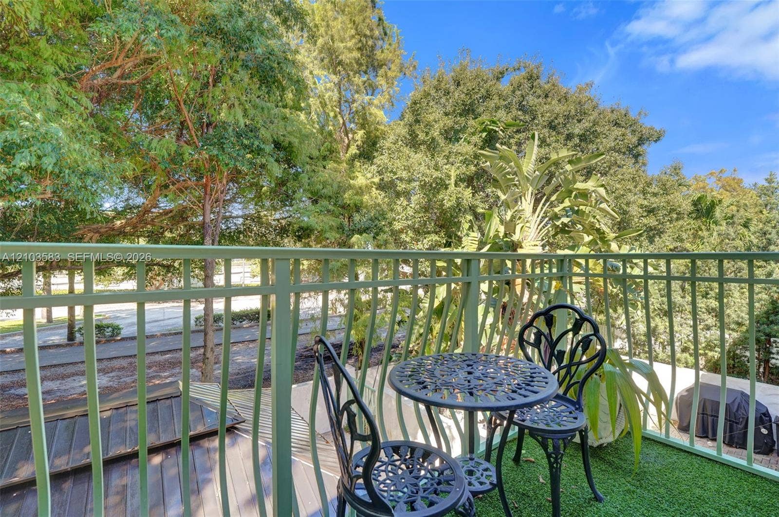 Balcony featuring green metal railing, artificial turf surfacing, and mature tree canopy