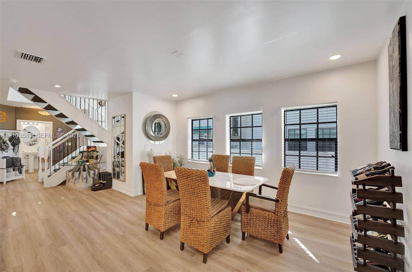 Open-concept dining area featuring wood-finish flooring, three windows with black-grid frames, and a custom staircase with metal railings