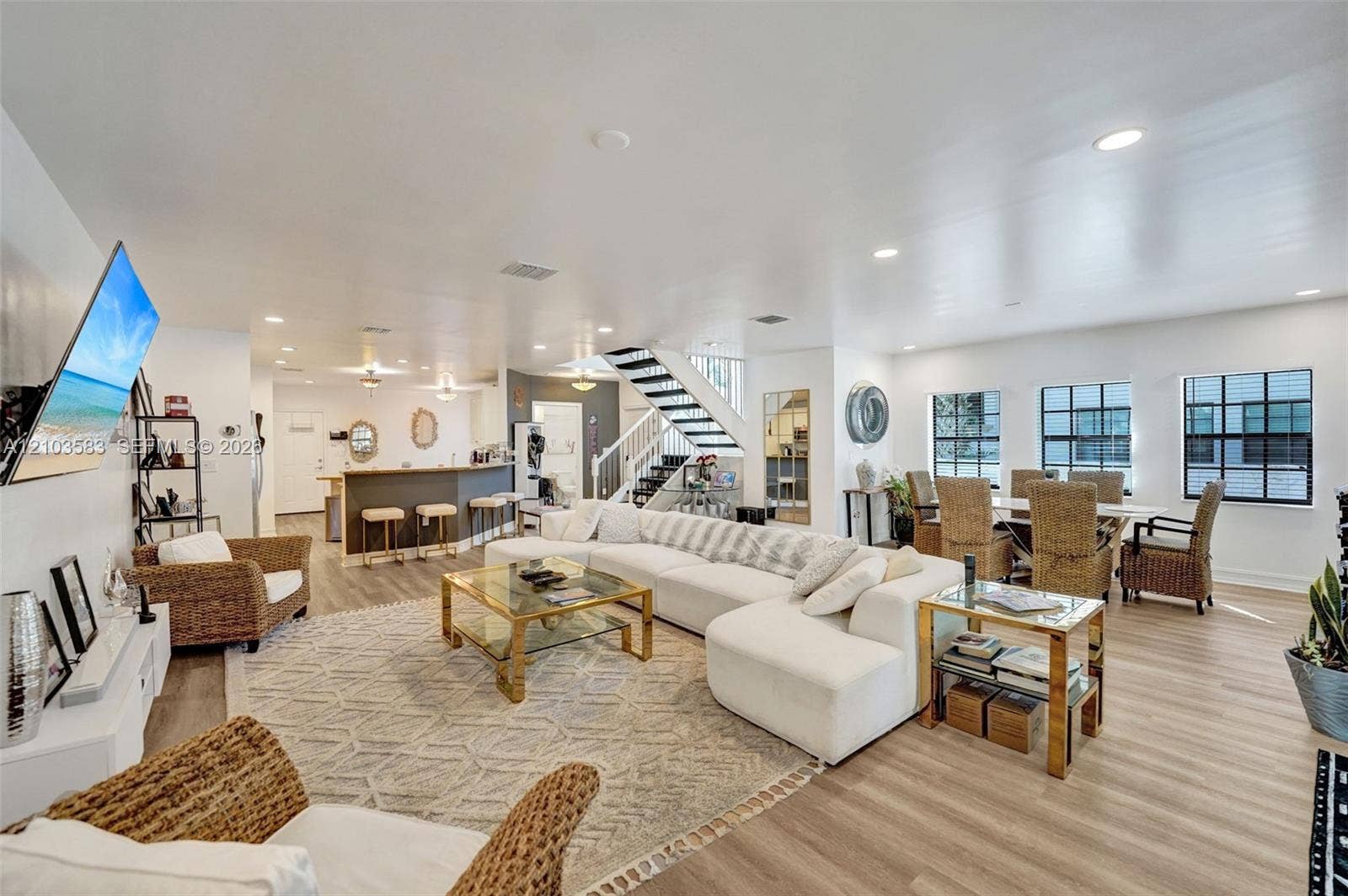 Open-concept interior featuring wood-finish flooring, recessed lighting, a breakfast bar, and a staircase with a black metal railing