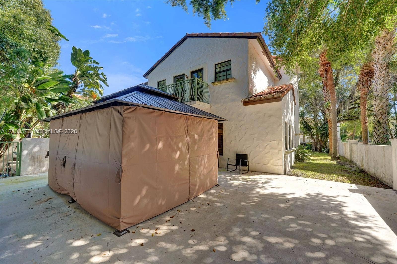 Stucco exterior featuring a second-story balcony with metal railing, a terracotta-tile roof, and a paved concrete patio area