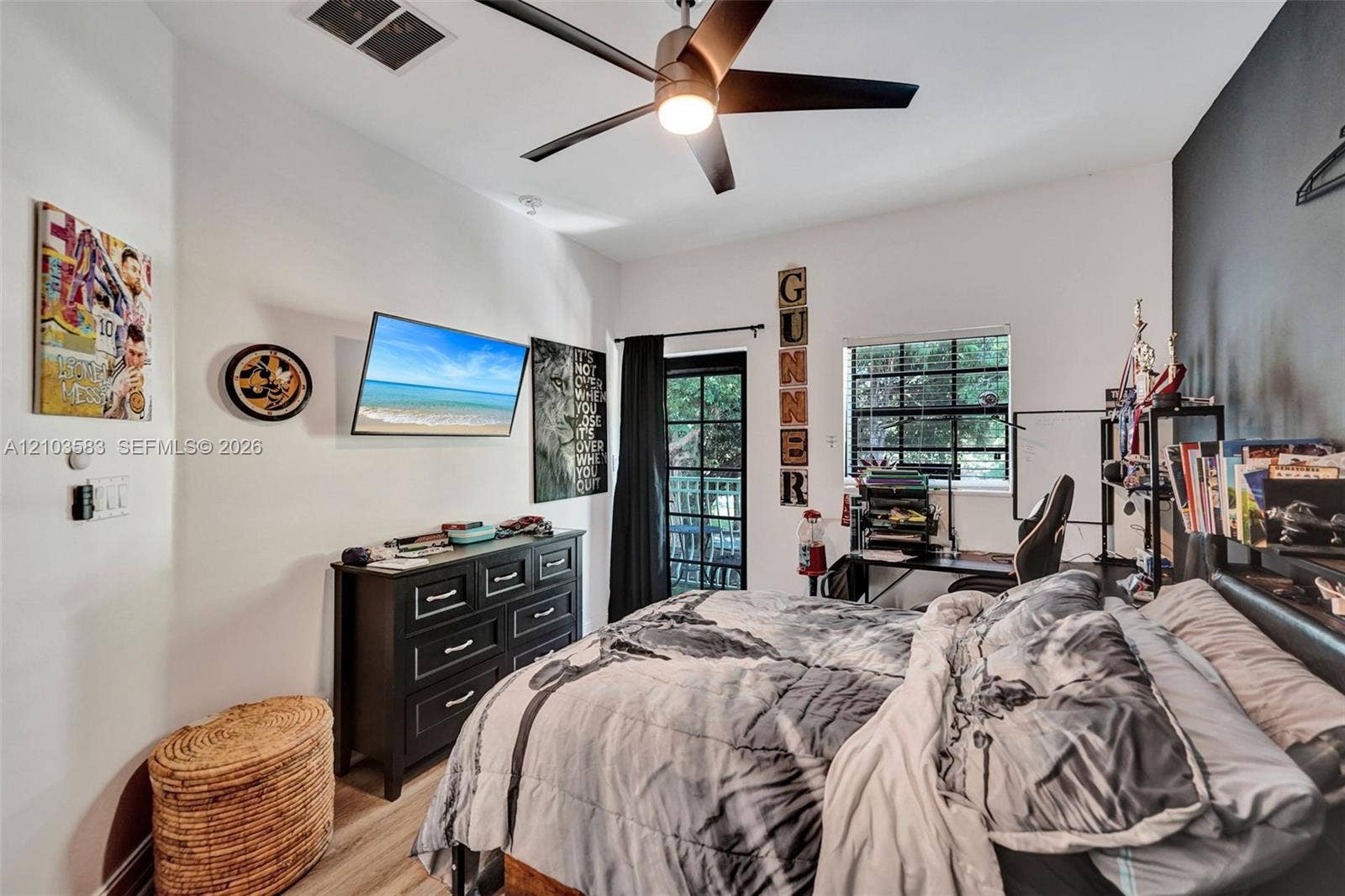 Room featuring wood-finish flooring, a matte black ceiling fan with integrated lighting, a dark accent wall, and a multi-lite door providing exterior access