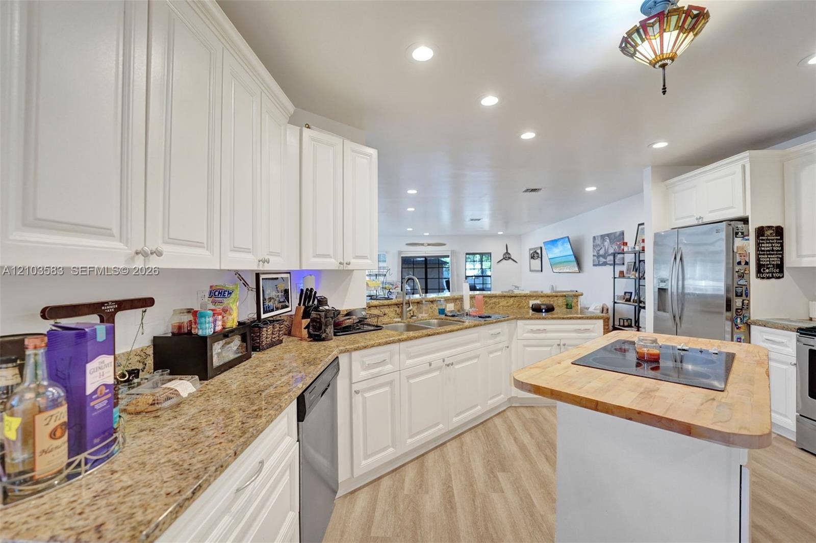 Kitchen featuring white shaker-style cabinetry, stone countertops, a central island with an integrated cooktop, stainless steel appliances, and wood-finish flooring