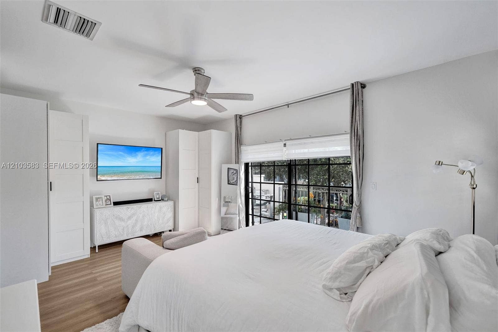 Bedroom featuring wood-finish flooring, built-in floor-to-ceiling cabinetry, a modern brushed-nickel ceiling fan, and black-framed glass sliding doors