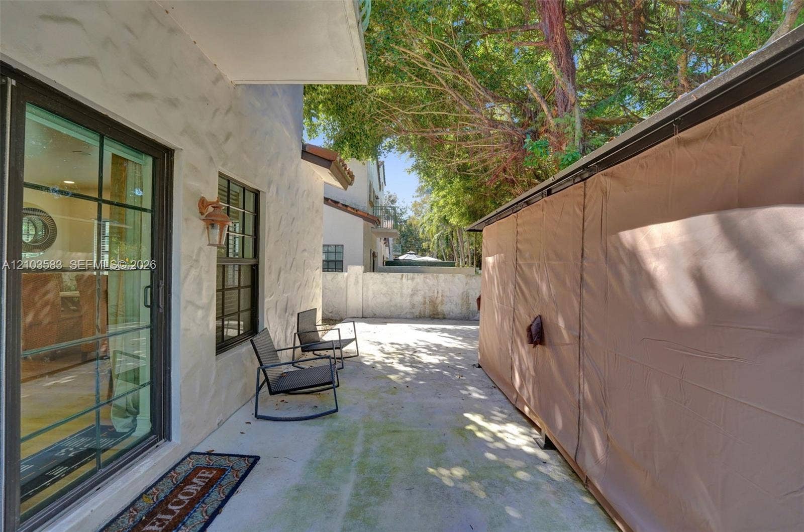 Paved patio area featuring textured stucco exterior wall, sliding glass doors, and wall-mounted exterior lighting