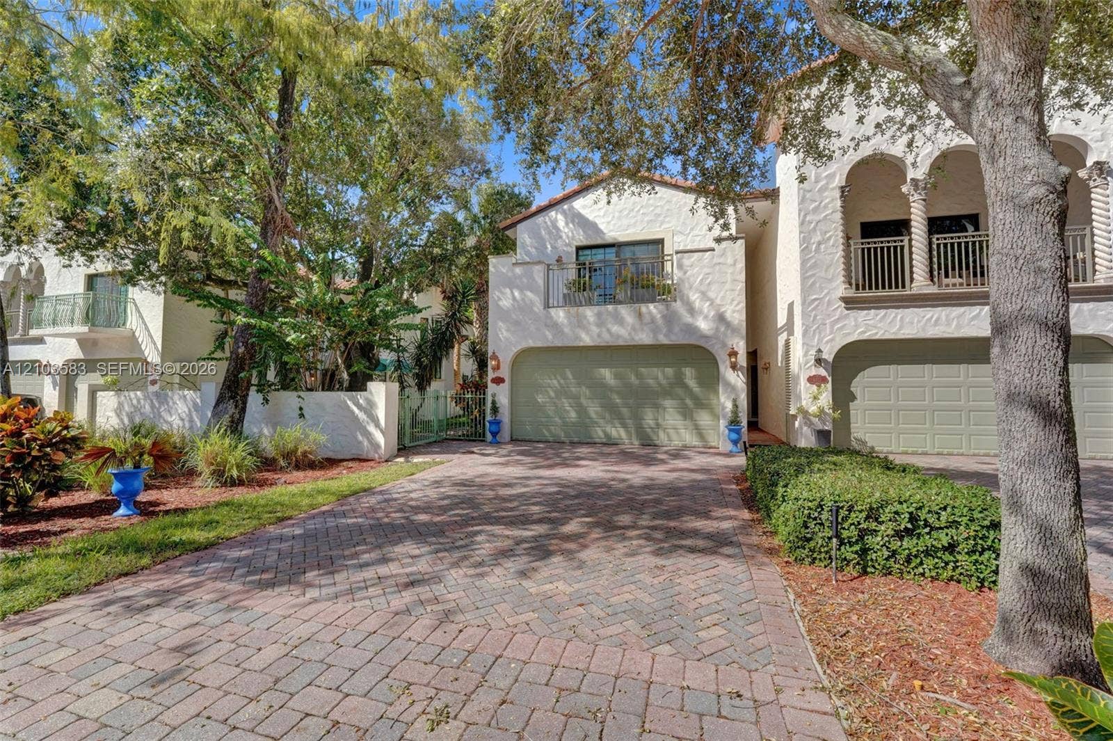 Stucco exterior featuring arched architectural detailing, herringbone-pattern paver driveway, second-story balconies with metal railings, and multi-car garage