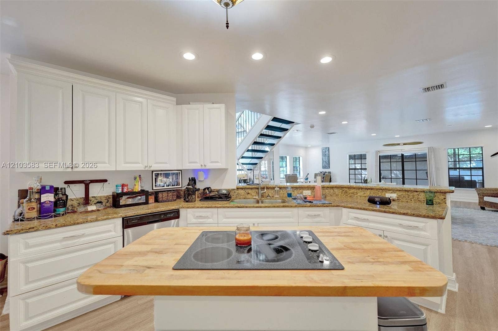 Kitchen featuring white cabinetry, stone countertops, central island with a wood-finish surface, integrated electric cooktop, and recessed lighting