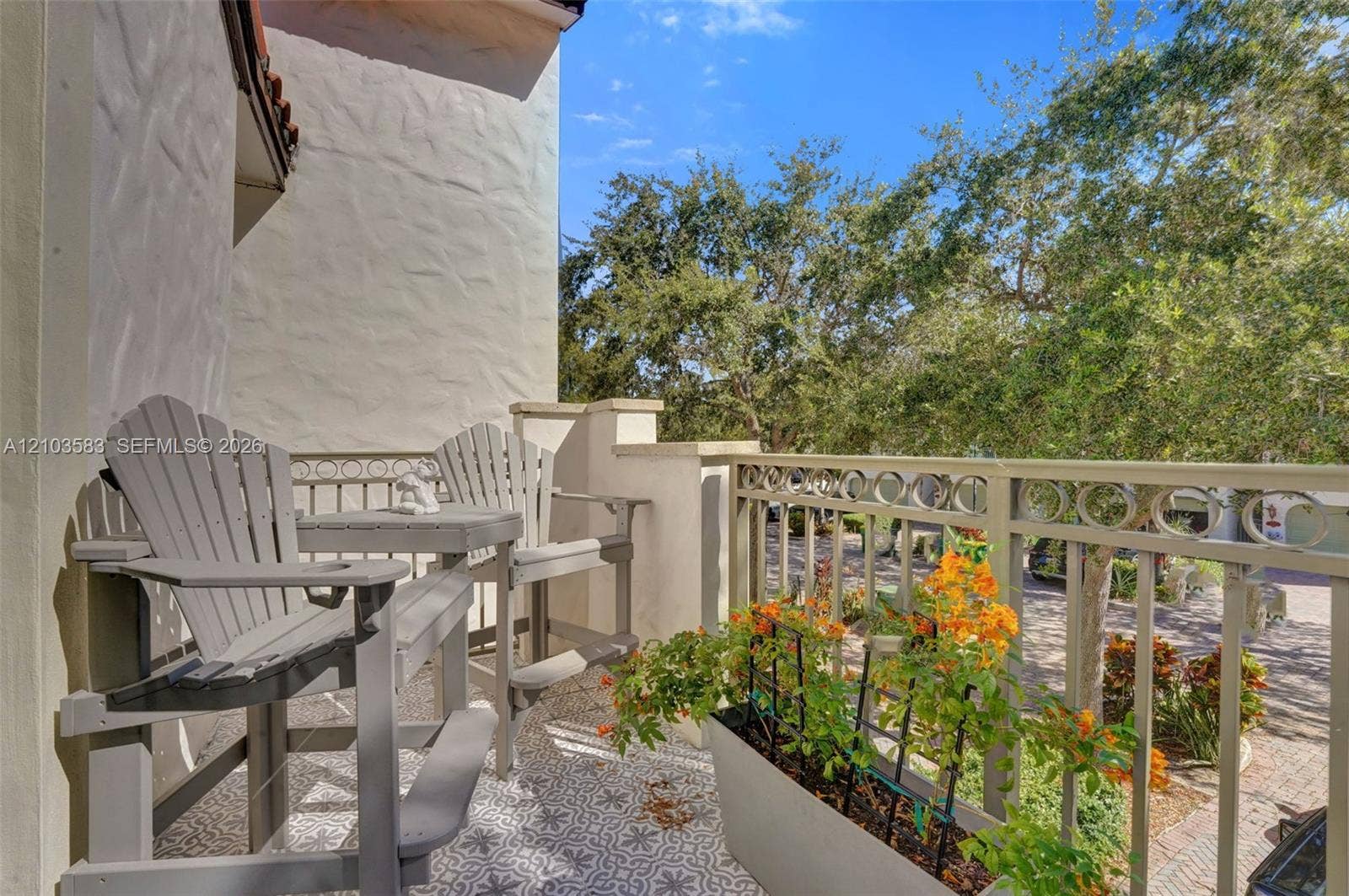 Exterior balcony featuring patterned tile flooring, textured stucco wall, and decorative metal railing