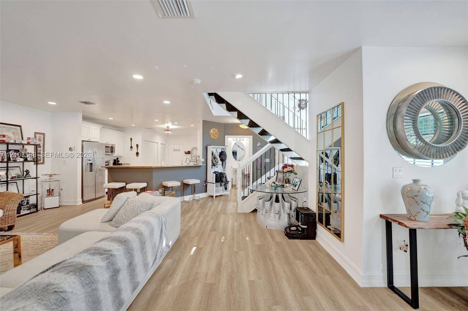 Open-concept interior featuring light-toned wood-finish flooring, recessed lighting, a kitchen breakfast bar with stone-finish countertops, and an architectural staircase with white railings and dark-toned treads