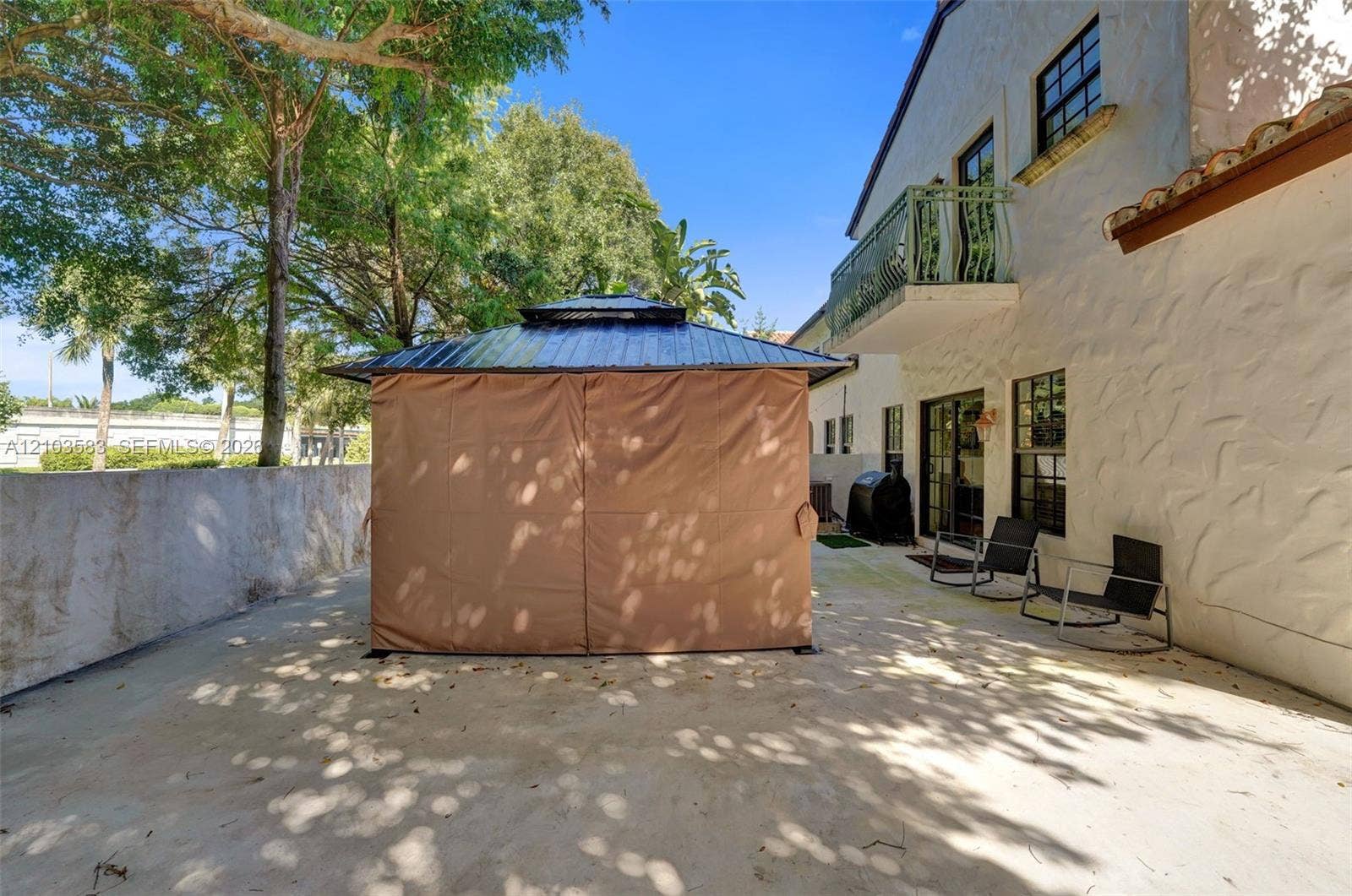 Concrete patio featuring a stucco exterior wall, second-story balcony with metal railing, and multi-pane windows