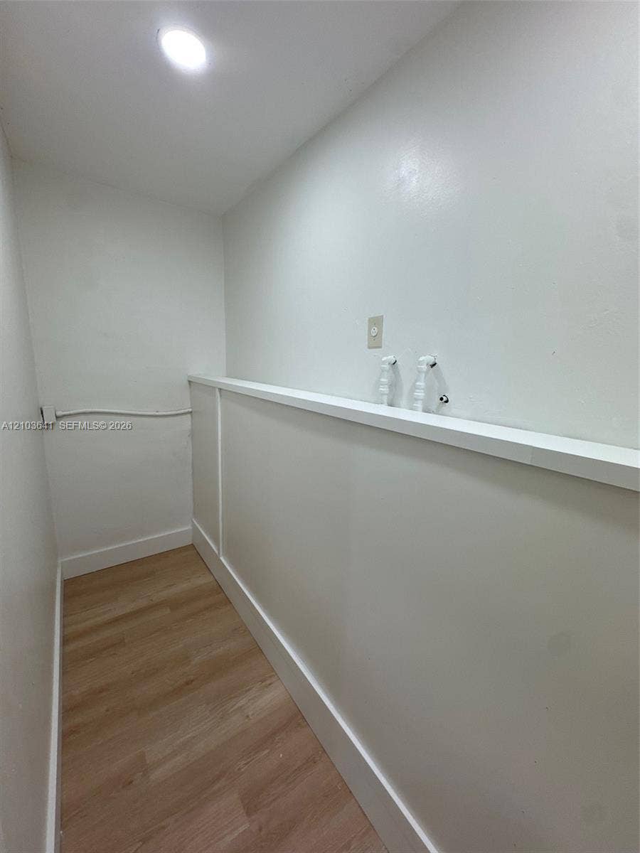 Utility area featuring wood-finish flooring, recessed ceiling lighting, and built-in plumbing connections with a mounted ledge