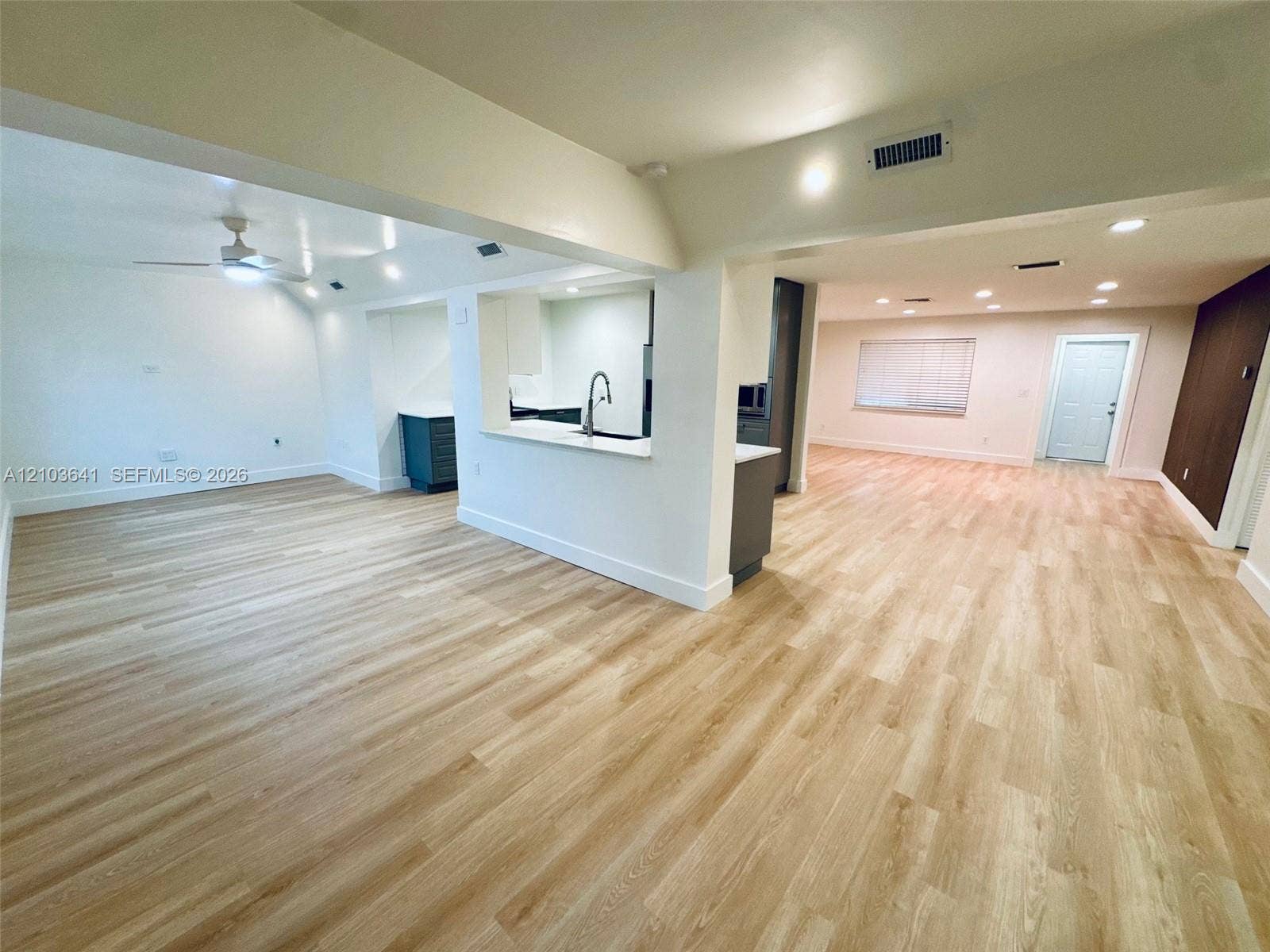 Open floor plan featuring wood-finish flooring, recessed lighting, ceiling fan, and a kitchen pass-through with a neutral countertop and single-handle faucet