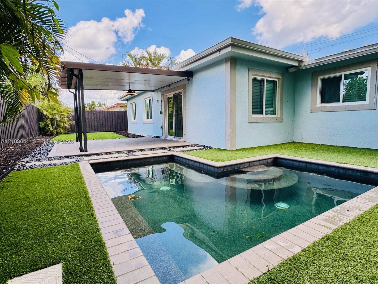 Outdoor space featuring an in-ground pool with stone coping, synthetic turf, a covered patio with a ceiling fan, and privacy fencing