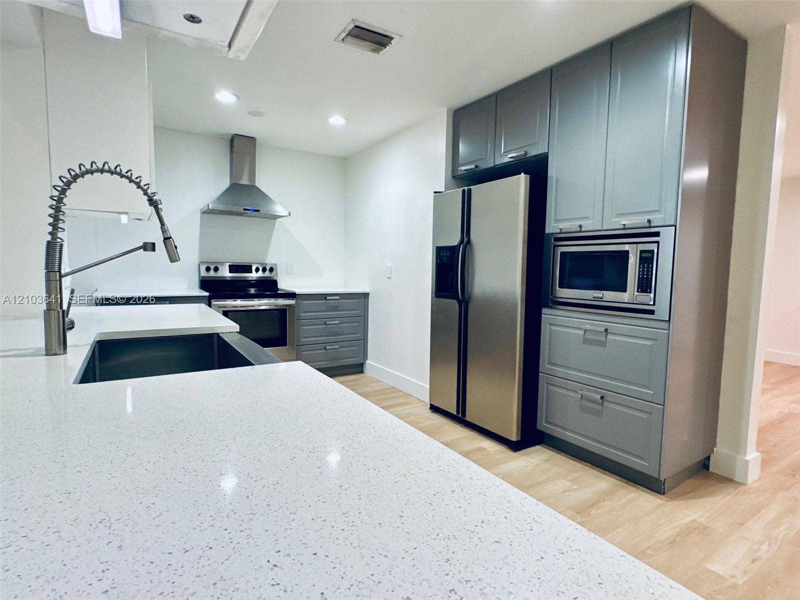 Kitchen featuring quartz countertops, gray cabinetry, stainless steel appliances, a professional-style pull-down faucet, and wood-finish flooring