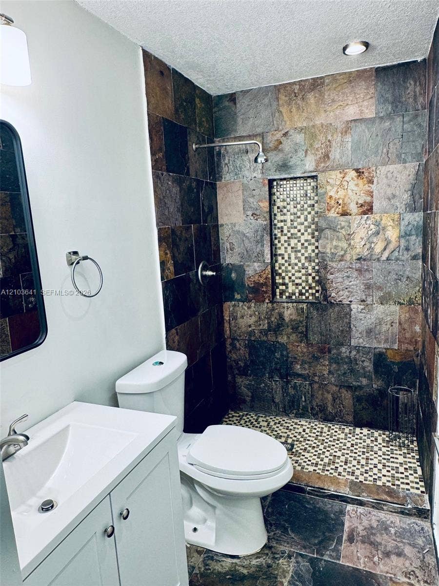 Stone-tile shower featuring a decorative mosaic inlay, walk-in design with mosaic tile flooring, vanity with integrated sink, and metal wall-mounted fixtures