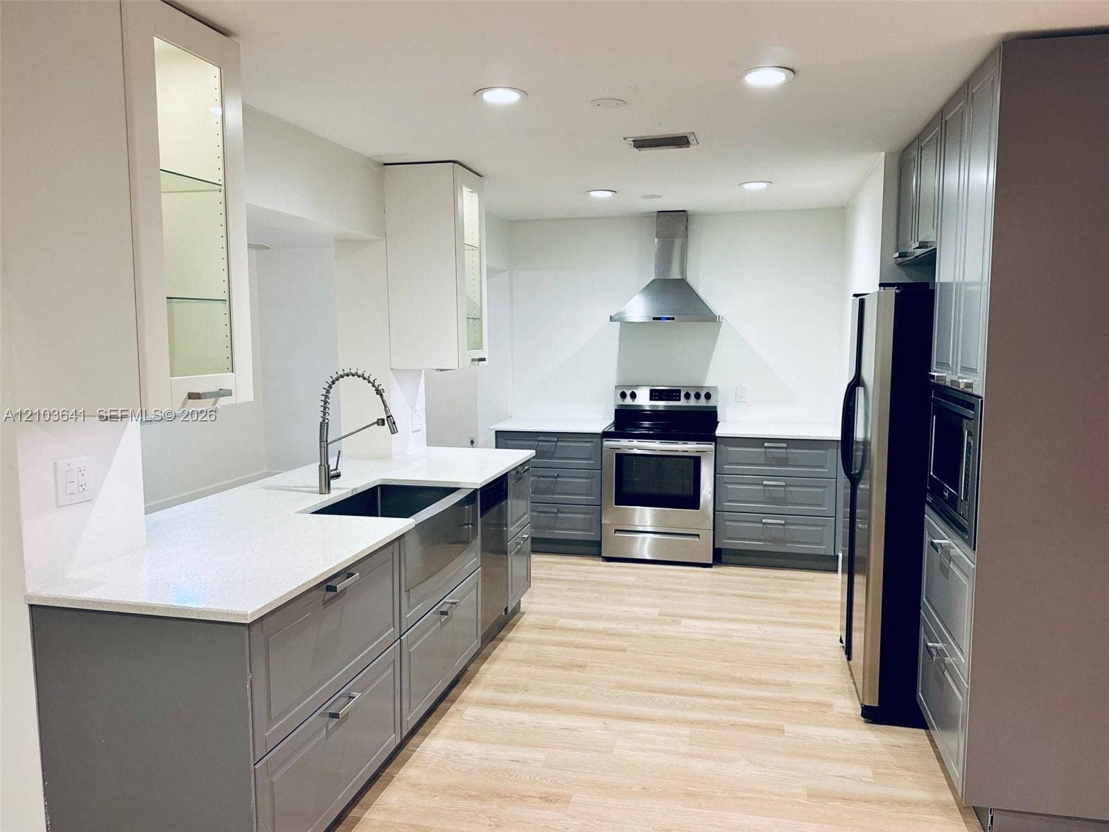 Kitchen featuring grey shaker-style cabinetry, white countertops, stainless steel appliances, a farmhouse sink with a pull-down faucet, and wood-finish flooring