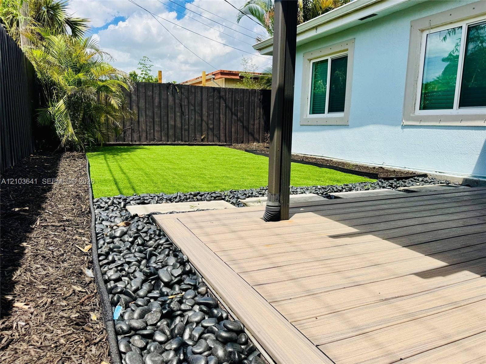 Composite deck featuring a synthetic turf lawn, bordered by polished black river rock landscaping and a tall privacy fence