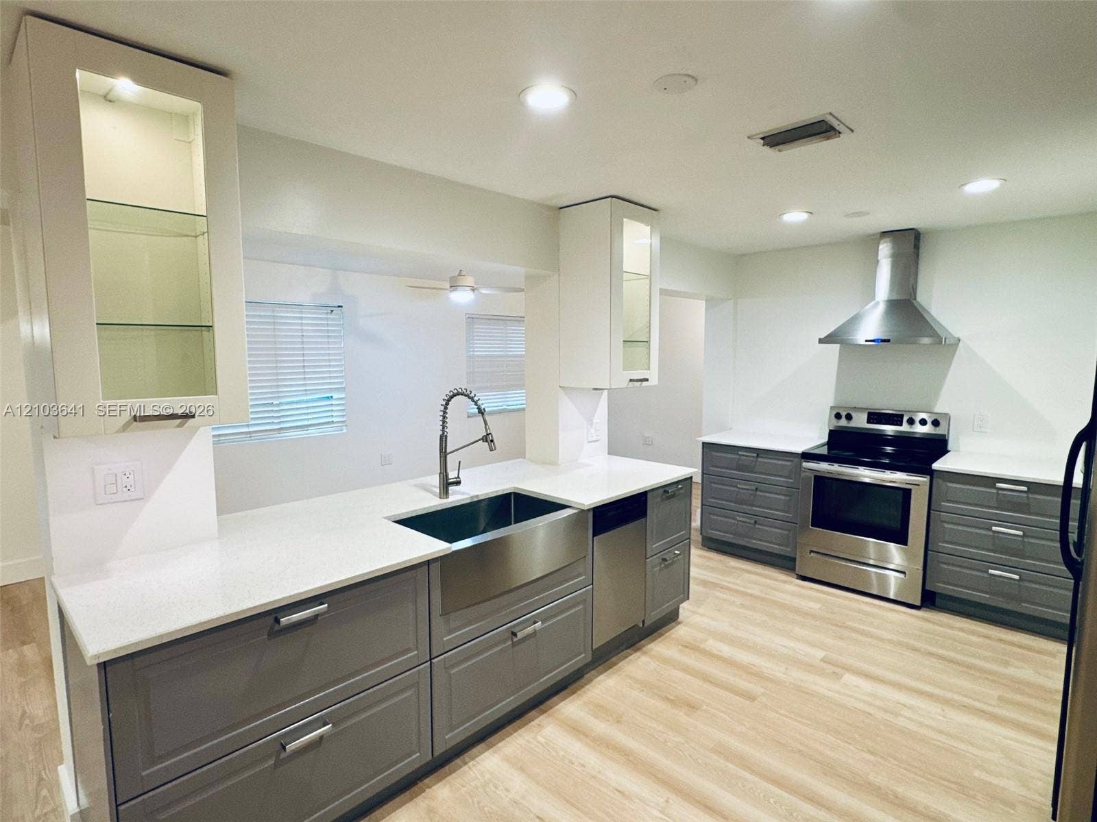 Kitchen featuring white quartz countertops, grey shaker-style cabinetry, stainless steel farmhouse-style sink, stainless steel range hood, and wood-finish flooring