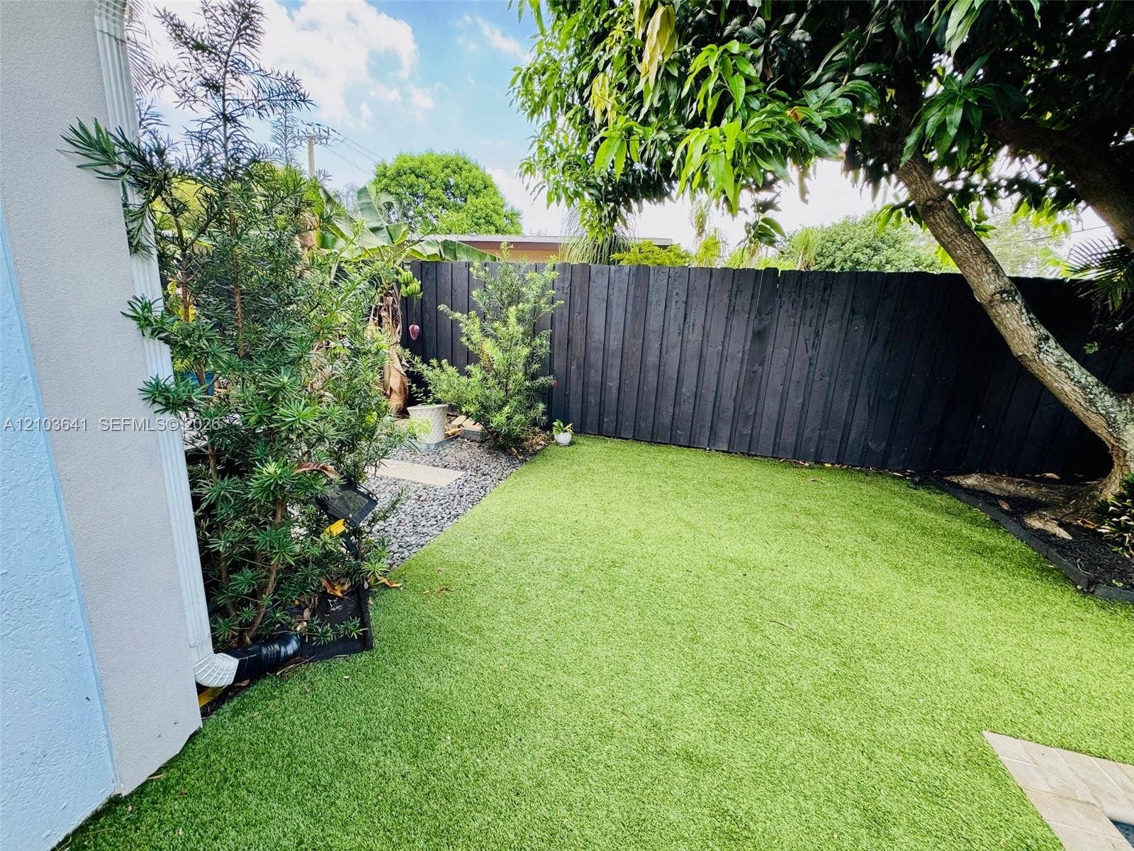 Fenced backyard featuring synthetic turf, stone-bordered landscaping, and mature trees