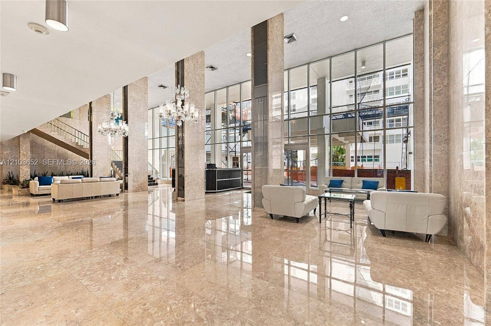 Expansive lobby featuring polished stone flooring, floor-to-ceiling glass walls, decorative chandeliers, and full-height stone-clad columns