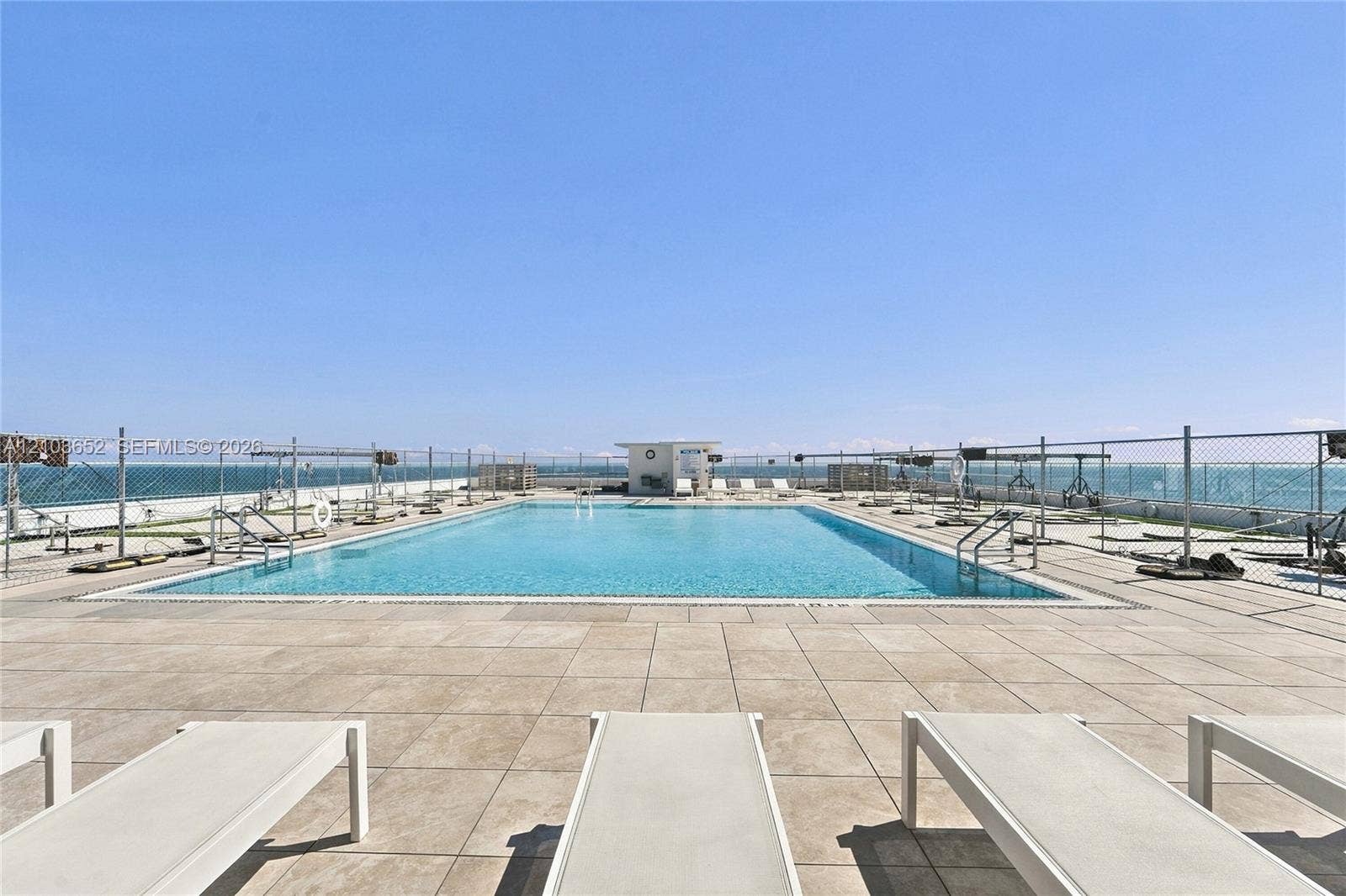 Rooftop swimming pool featuring large-format tile decking, metal perimeter fencing, and stainless steel pool ladders