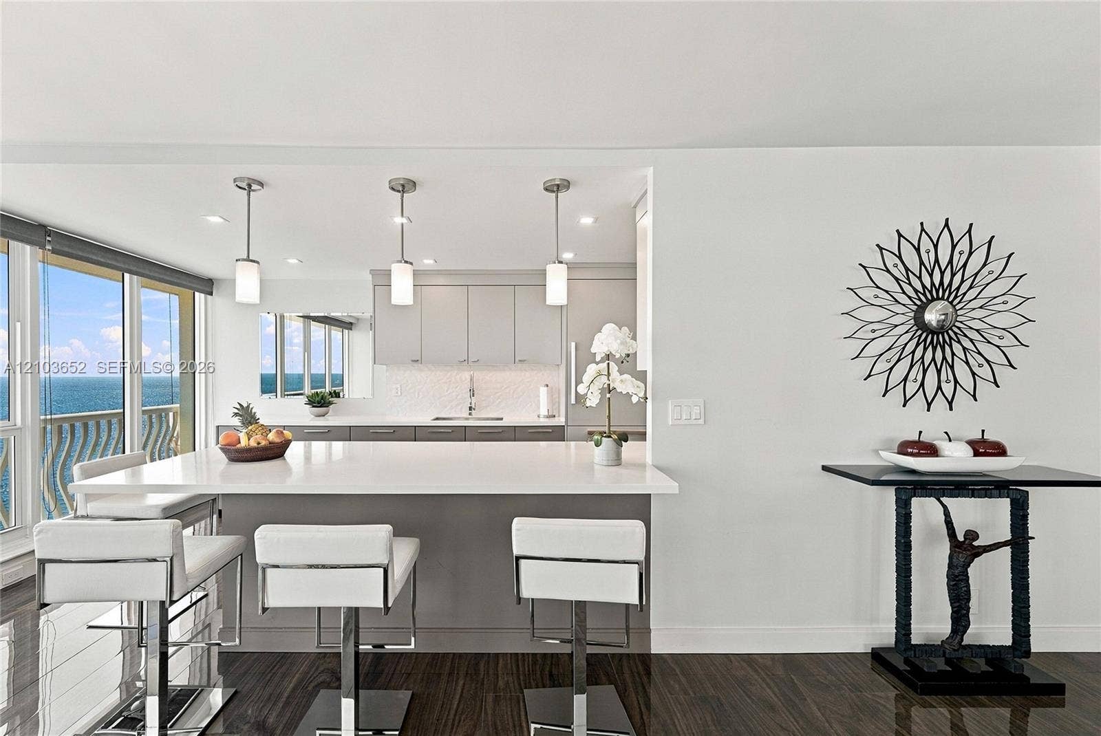 Kitchen featuring a waterfall-edge island with seating, grey cabinetry, textured backsplash, and three cylindrical pendant lights, finished with dark wood-finish flooring