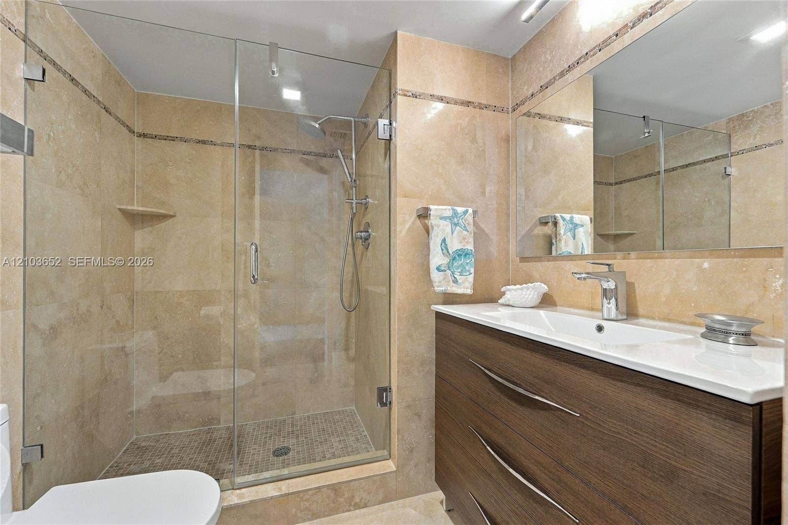 Bathroom featuring a walk-in shower with glass enclosure, wall-mounted shower head, wood-finish vanity with a white countertop, and oversized mirror