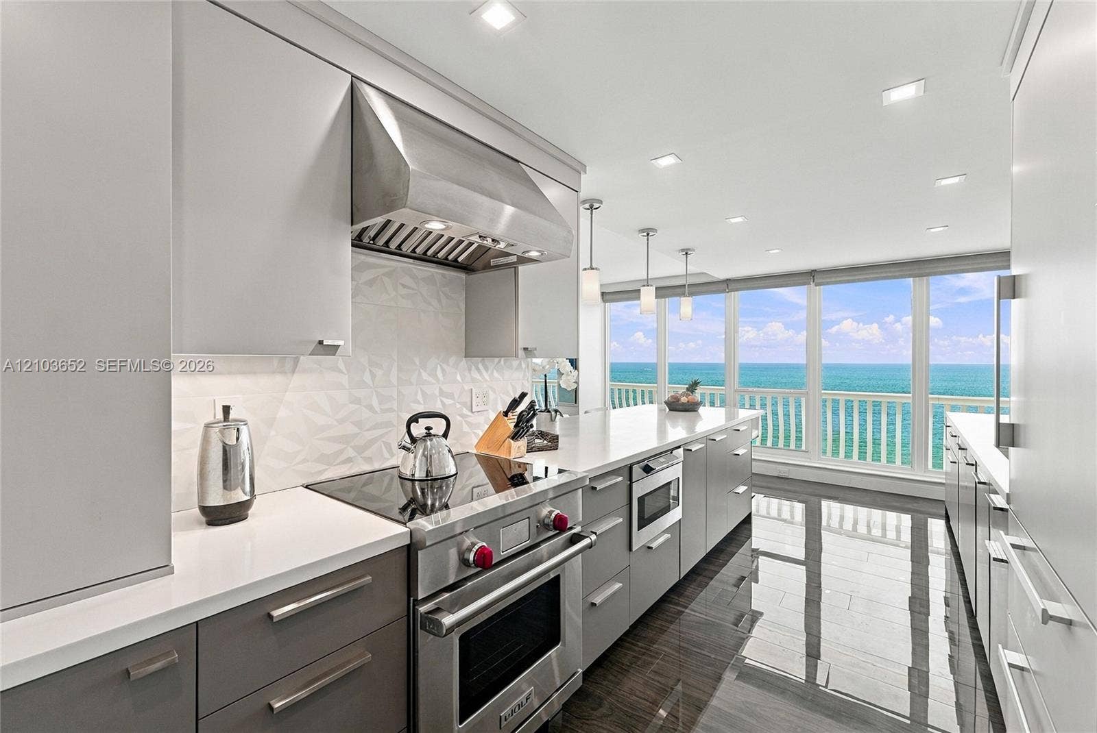 Modern kitchen featuring sleek two-tone cabinetry, professional-grade stainless steel range, geometric tile backsplash, stone countertops, and floor-to-ceiling windows with water exposure