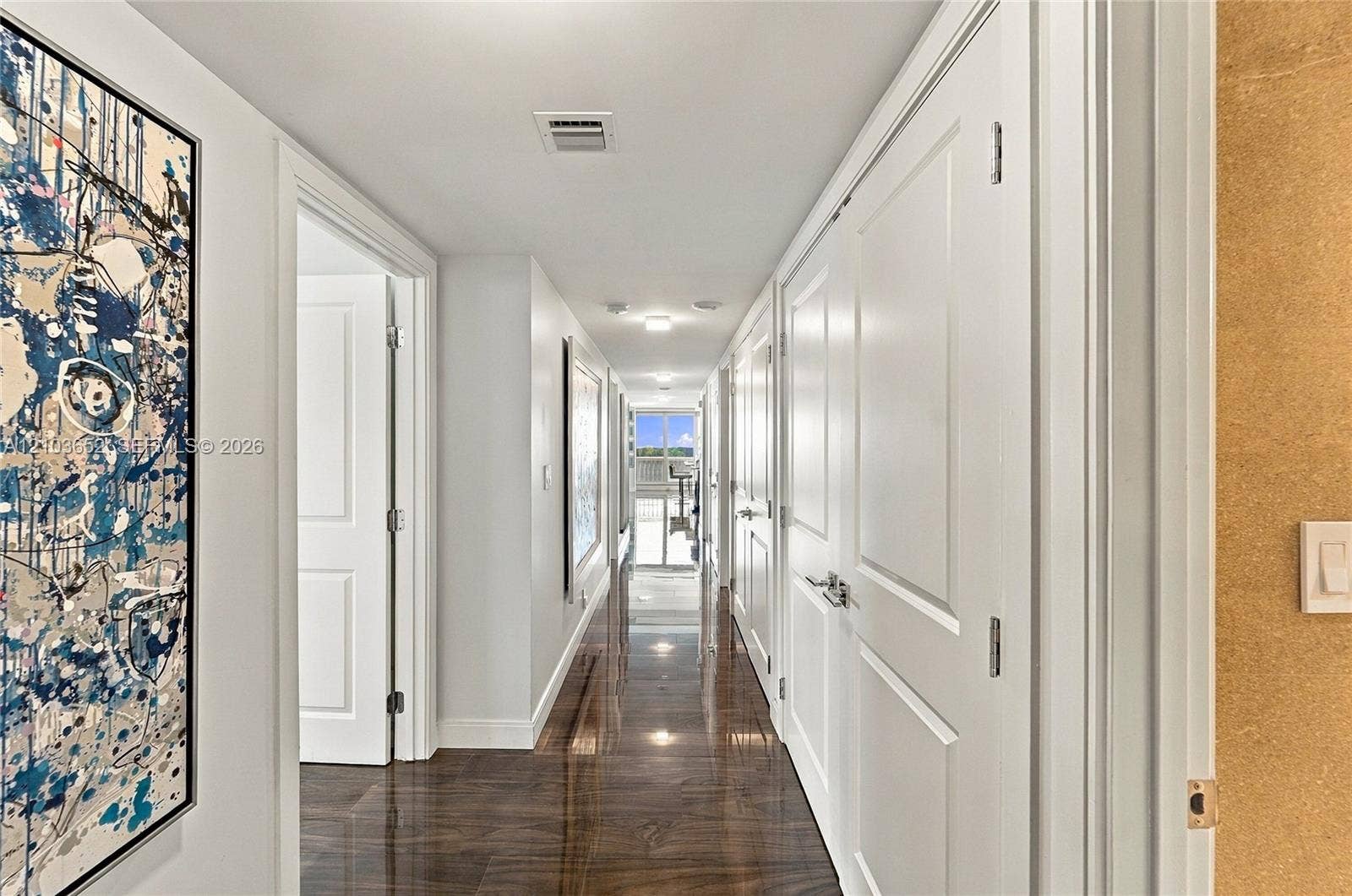 Hallway featuring dark wood-finish flooring, crisp white walls, and multiple solid-core interior doors with satin nickel hardware