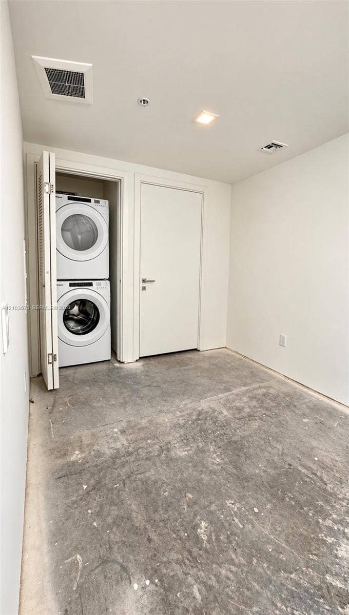 Stacked laundry unit with white appliances, enclosed within a closet featuring bi-fold doors, complemented by recessed ceiling lighting and a flat-panel interior door