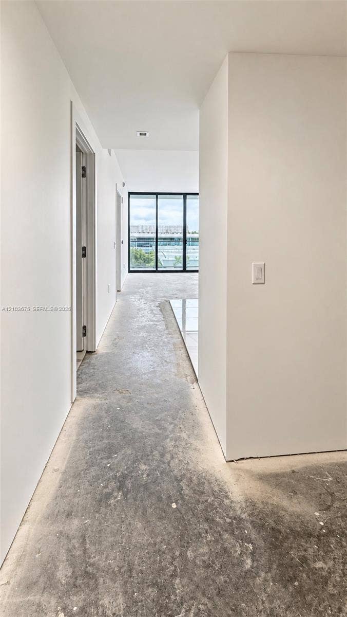 Interior hallway featuring floor-to-ceiling black-framed glass panels, recessed ceiling lighting, and polished stone tile flooring