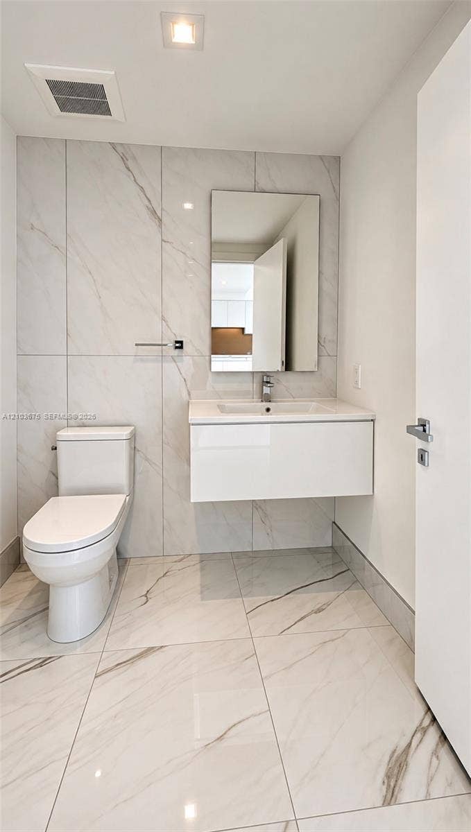 Floating vanity with a white integrated basin, floor-to-ceiling large-format tile wall, white stone-patterned floor tiling, rectangular mirror, and chrome single-handle faucet