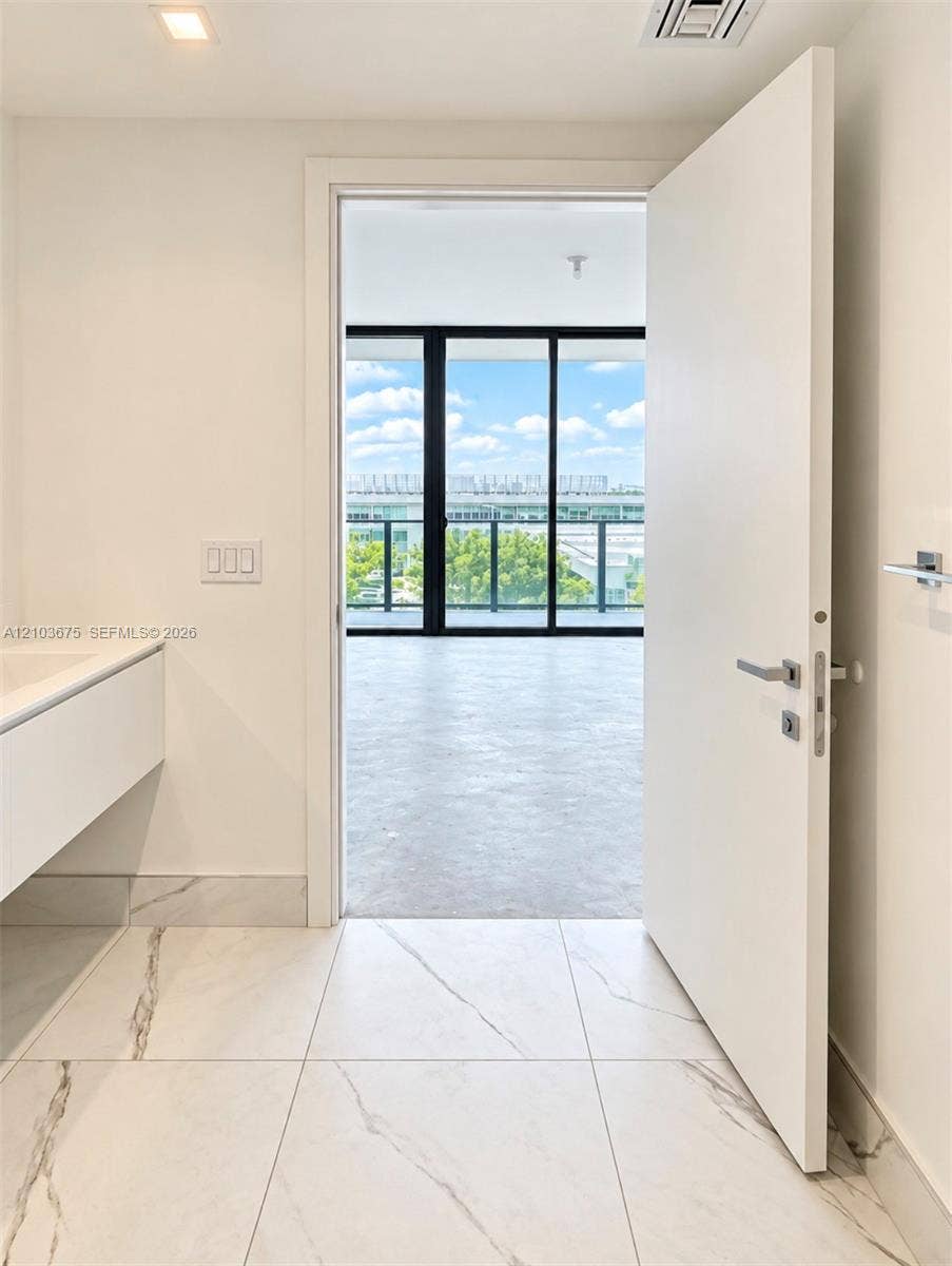 Large-format tile flooring with marble-style veining, floating vanity cabinet, and expansive floor-to-ceiling glass sliding doors with black framing