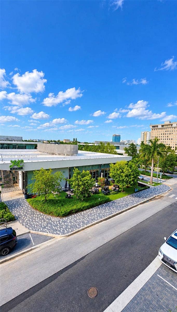 Commercial property featuring a flat roofline, floor-to-ceiling glass paneling, patterned paver walkways, and established green space with mature landscaping