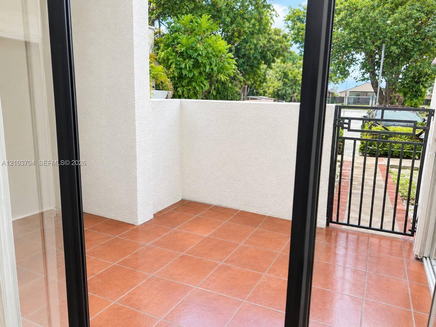 Private outdoor patio featuring terracotta-style tile flooring, high stucco privacy walls, and a secure metal gate entry