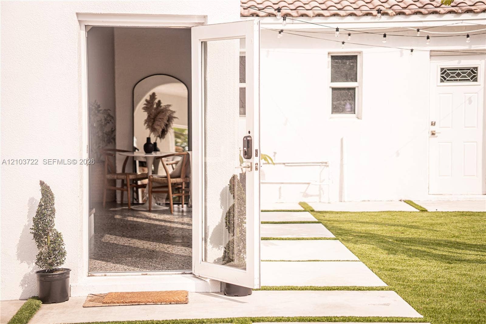 White exterior stucco finish, full-lite glass door, concrete paver pathway, and synthetic turf lawn