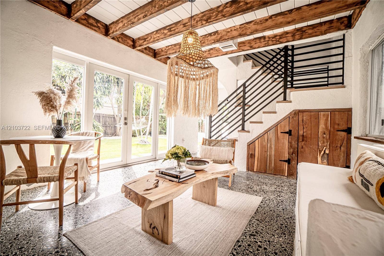 Exposed wooden ceiling beams, terrazzo flooring, custom under-stair wood cabinetry, black metal staircase railing, and glass paneled exterior doors