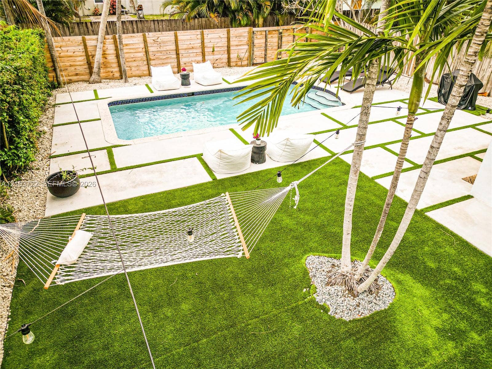 Backyard featuring an inground swimming pool, concrete pavers with turf infill, synthetic turf lawn, mature palm trees, and wood-panel privacy fencing