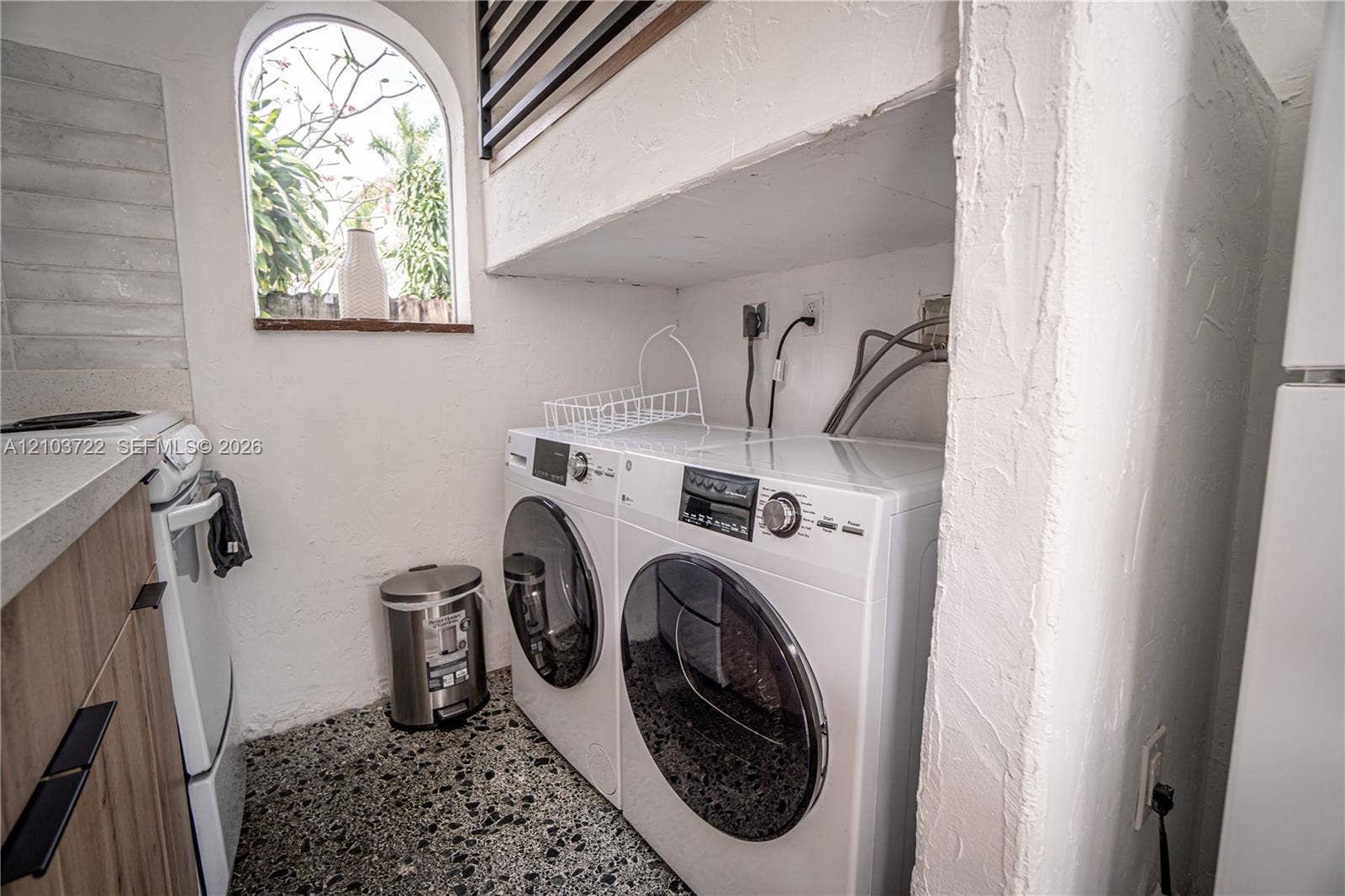 Laundry area featuring stone-aggregate flooring, arched window, wood-finish cabinetry, and solid-surface countertops