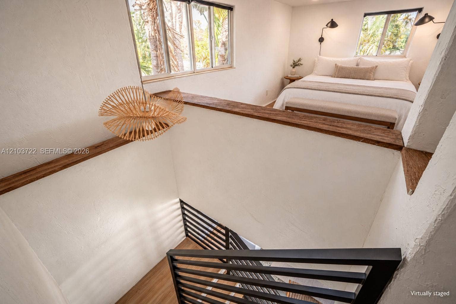 Black metal stair railing with horizontal balusters, natural wood-finish ledge caps, textured white walls, and wood-finish flooring