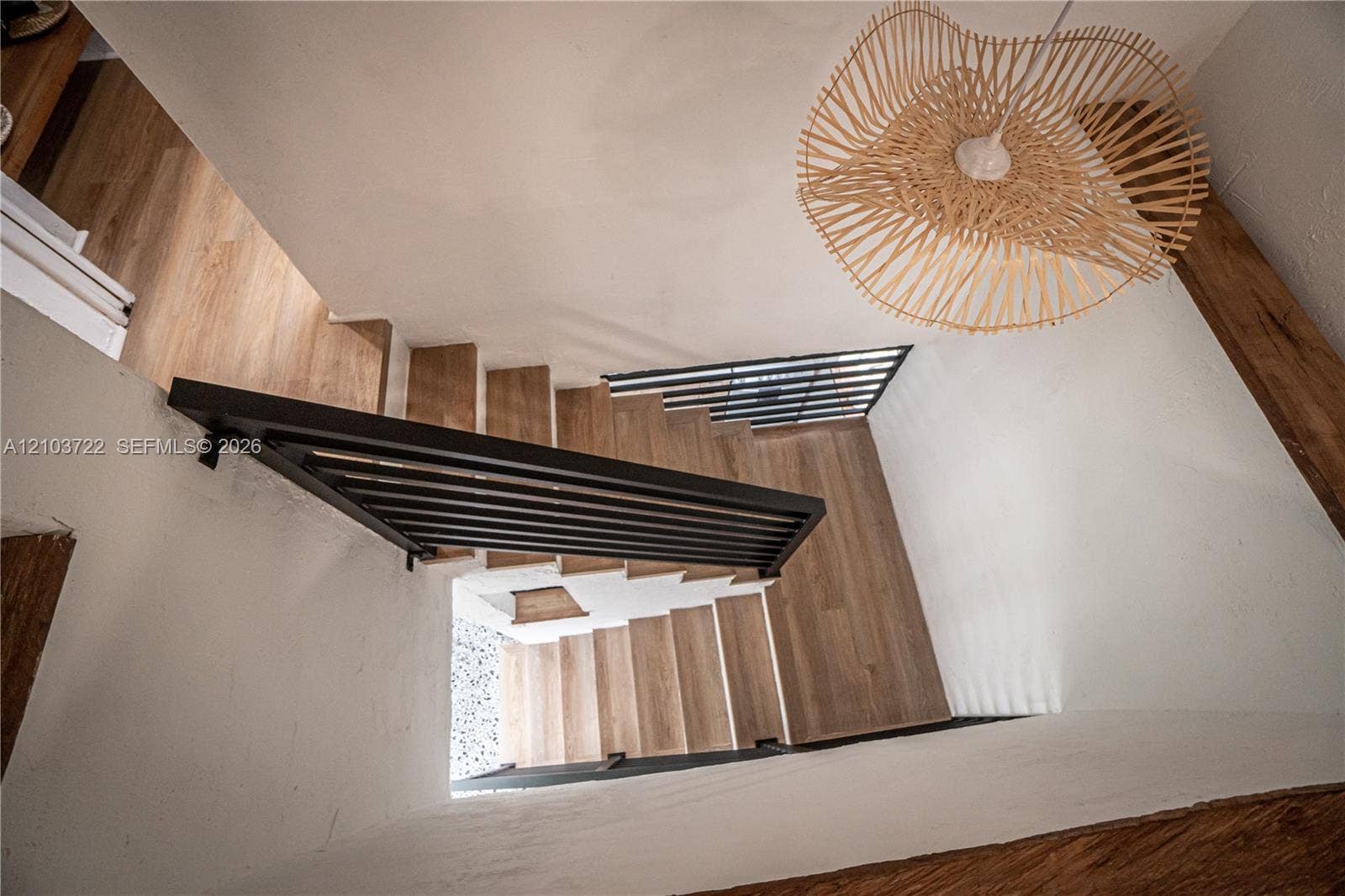 Staircase featuring wood-finish treads, matte black horizontal railings, and a woven pendant light fixture