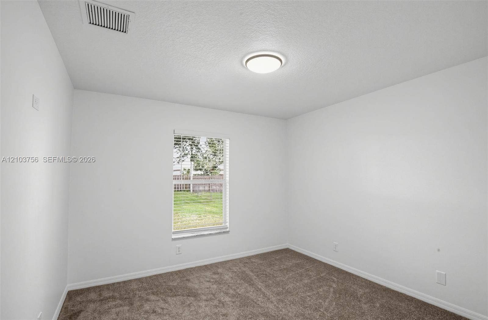 Neutral-toned carpeting, crisp white wall finish, flush-mount circular lighting fixture, and a single-pane window with horizontal blinds
