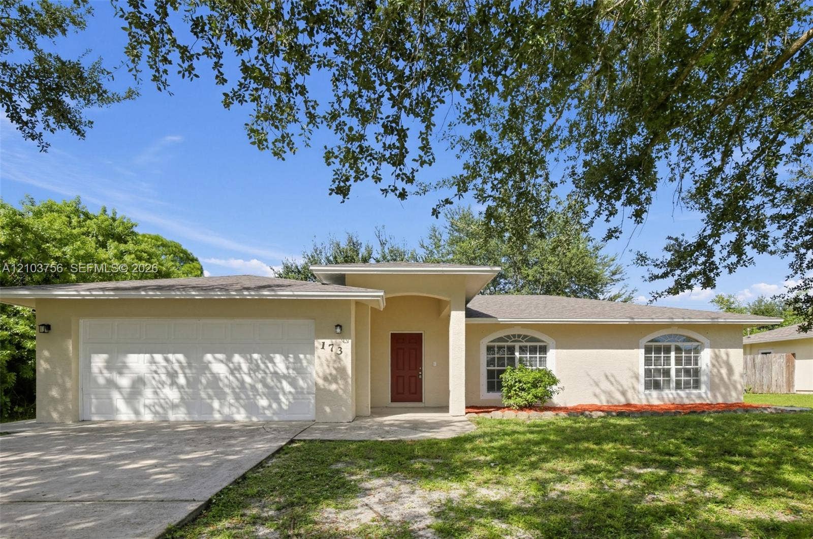 Single-story exterior featuring light-toned stucco siding, an attached two-car garage, an arched entryway, and multiple windows with decorative arched transoms