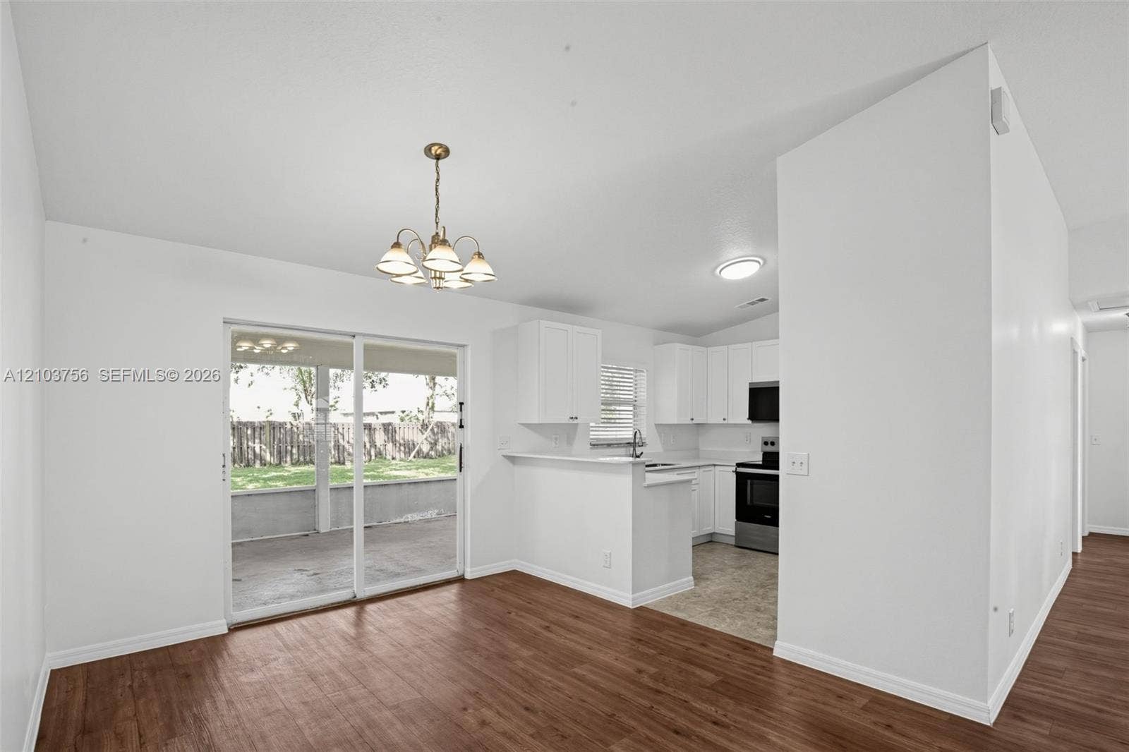 Open-concept space featuring wood-finish flooring, a multi-light chandelier, and a sliding glass door providing external access