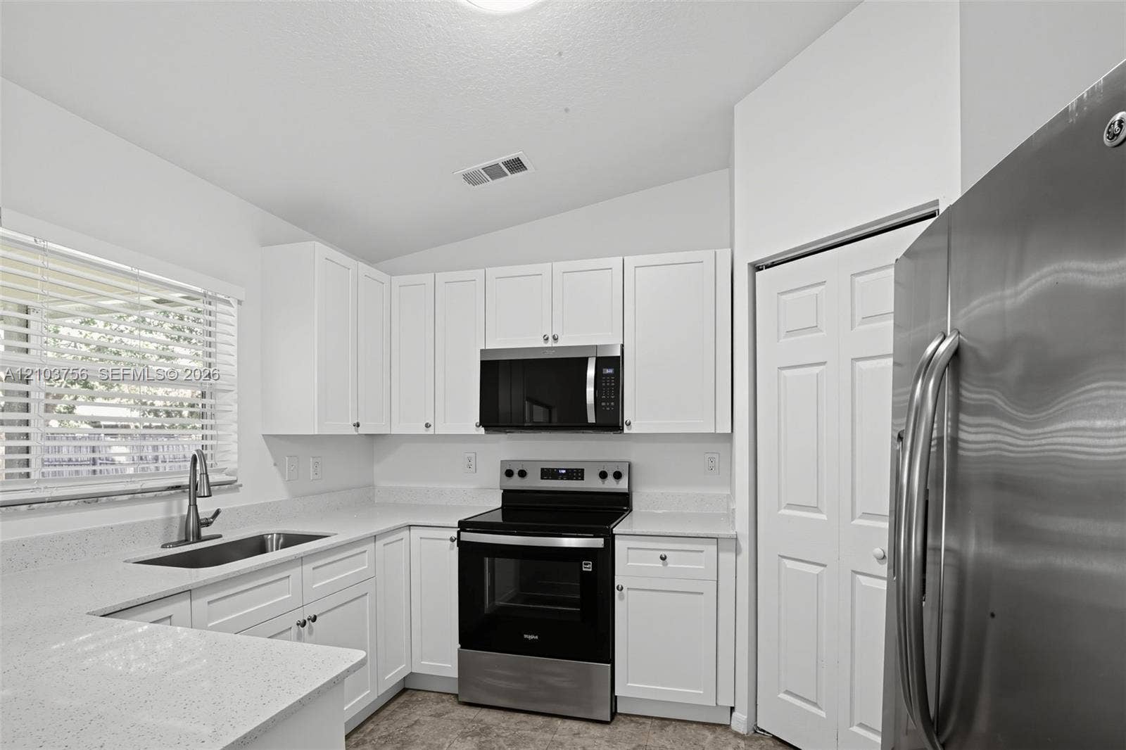Kitchen featuring white shaker-style cabinetry, white countertops, stainless steel appliances, a stainless steel undermount sink with a pull-down faucet, and neutral flooring