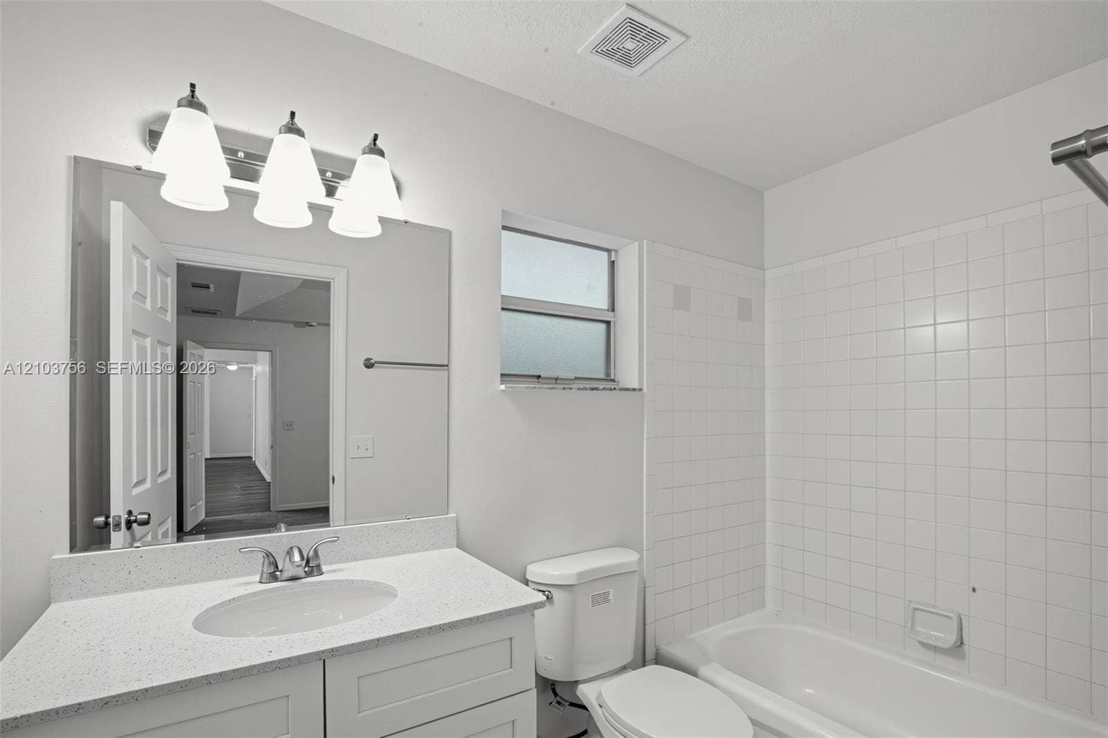 Bathroom featuring a vanity with a white countertop and oval under-mount sink, three-light fixture, wall-mounted mirror, and white tile tub surround