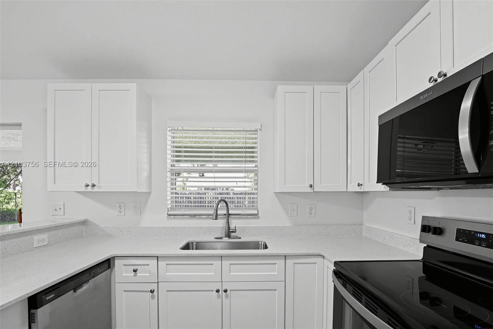 Kitchen featuring white shaker-style cabinetry, solid-surface countertops, undermount stainless steel sink with high-arc faucet, and stainless steel appliances