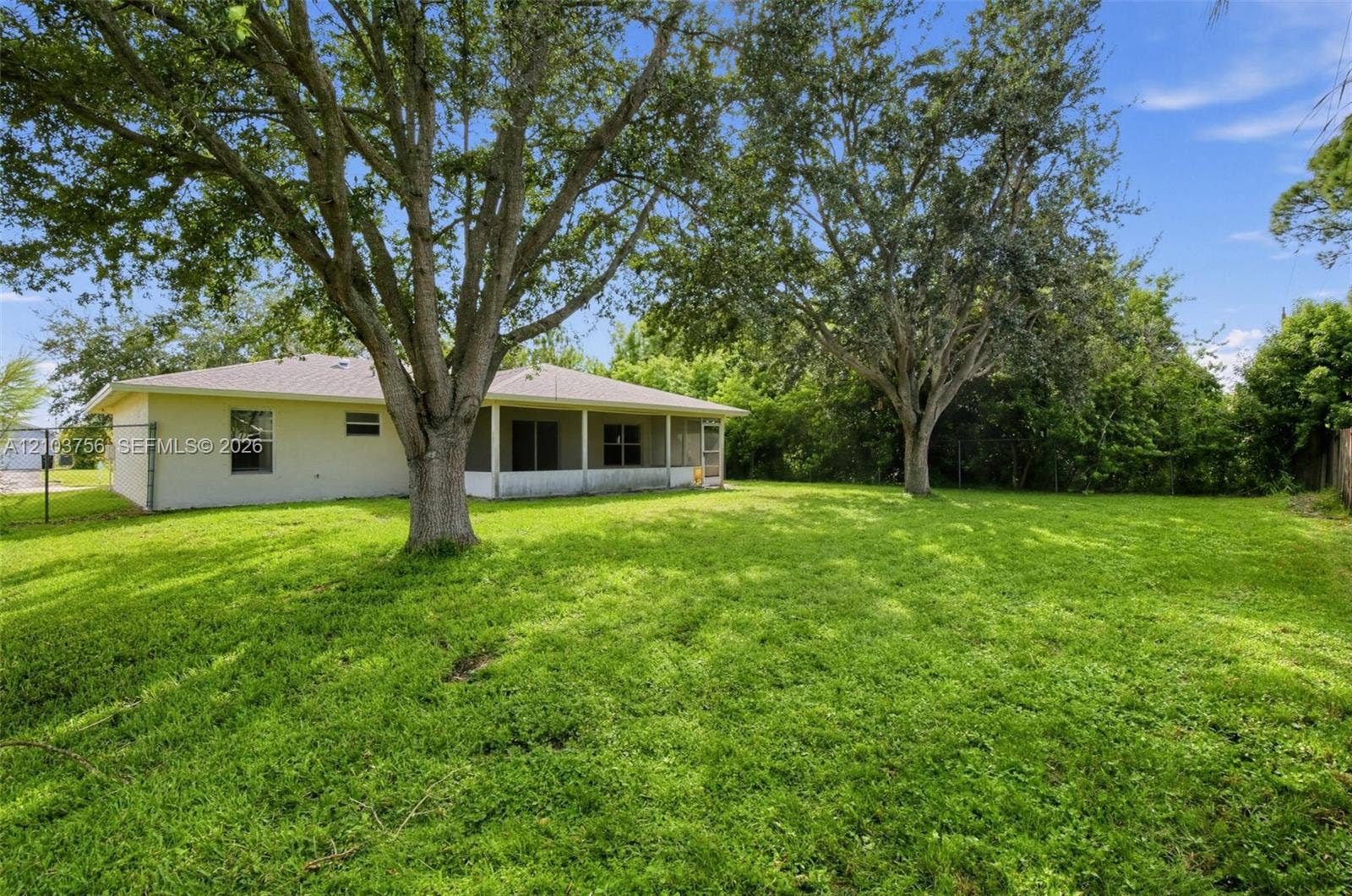 Spacious backyard featuring mature trees, a covered patio with screening, and light-colored stucco exterior siding
