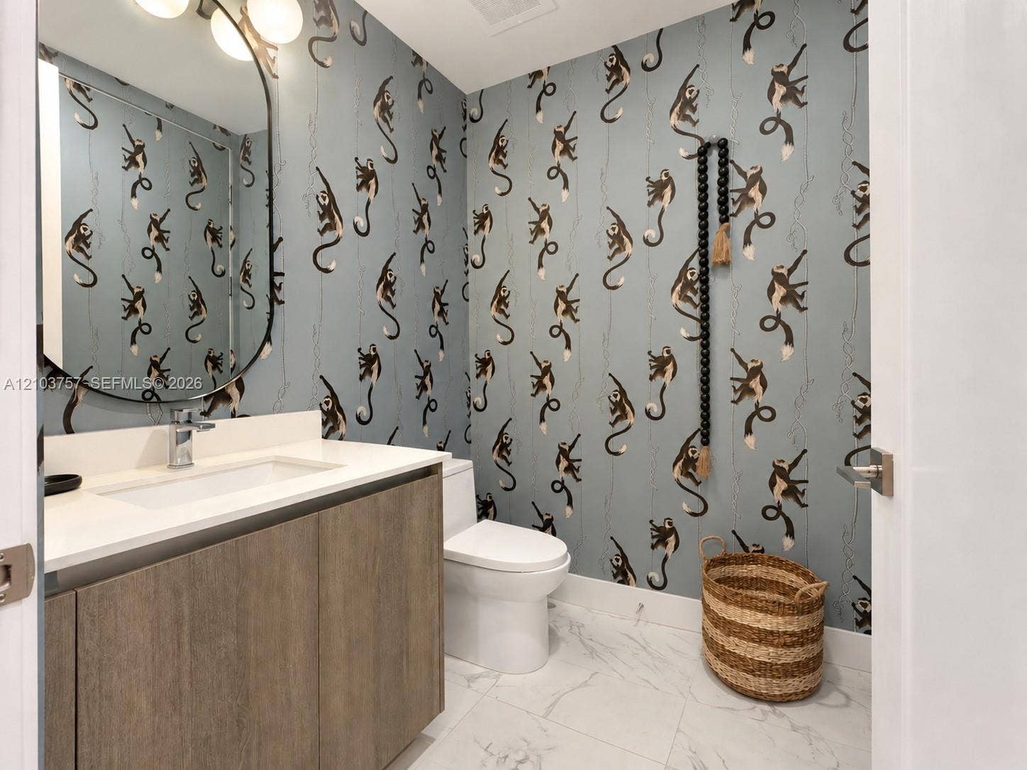 17550 Collins Avenue, #1103, Sunny Isles Beach, Sunny Isles Beach, FL 33160 Wood-finish vanity with an integrated rectangular sink, wall-mounted oval mirror, and a three-light vanity fixture