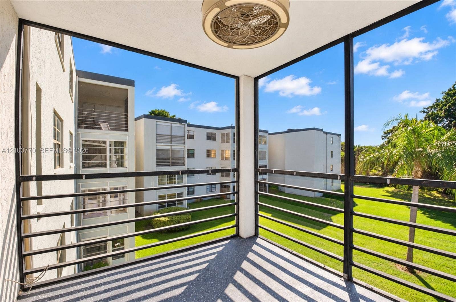 9440 SW 8th Street, #309, Boca Raton, Boca Raton, FL 33428 Screened balcony with a mounted ceiling fan, textured flooring, and black metal railings overlooking a landscaped green space