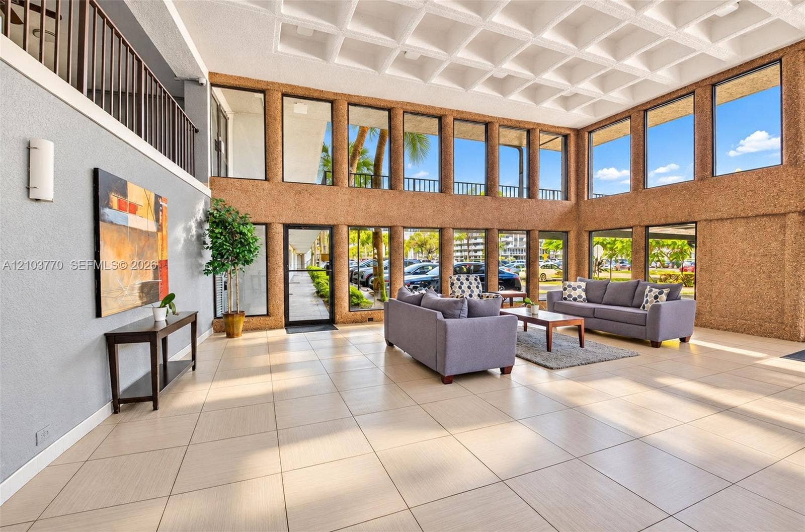 9440 SW 8th Street, #309, Boca Raton, Boca Raton, FL 33428 Spacious common area featuring a coffered ceiling, two-story window walls, ceramic tile flooring, and a second-story interior balcony with an iron railing